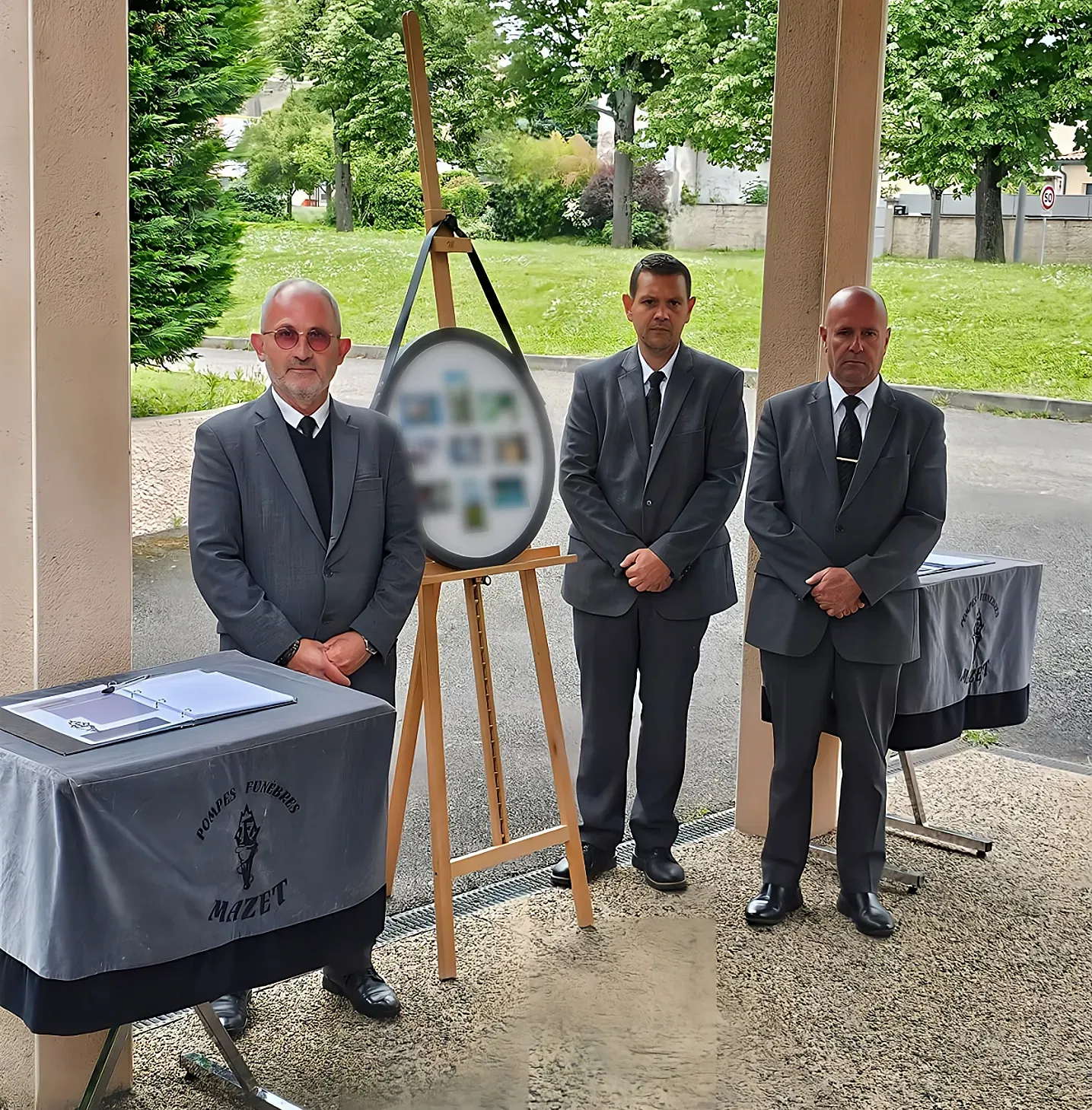 Trois porteurs funéraires en costume gris posant devant une entrée de bâtiment.