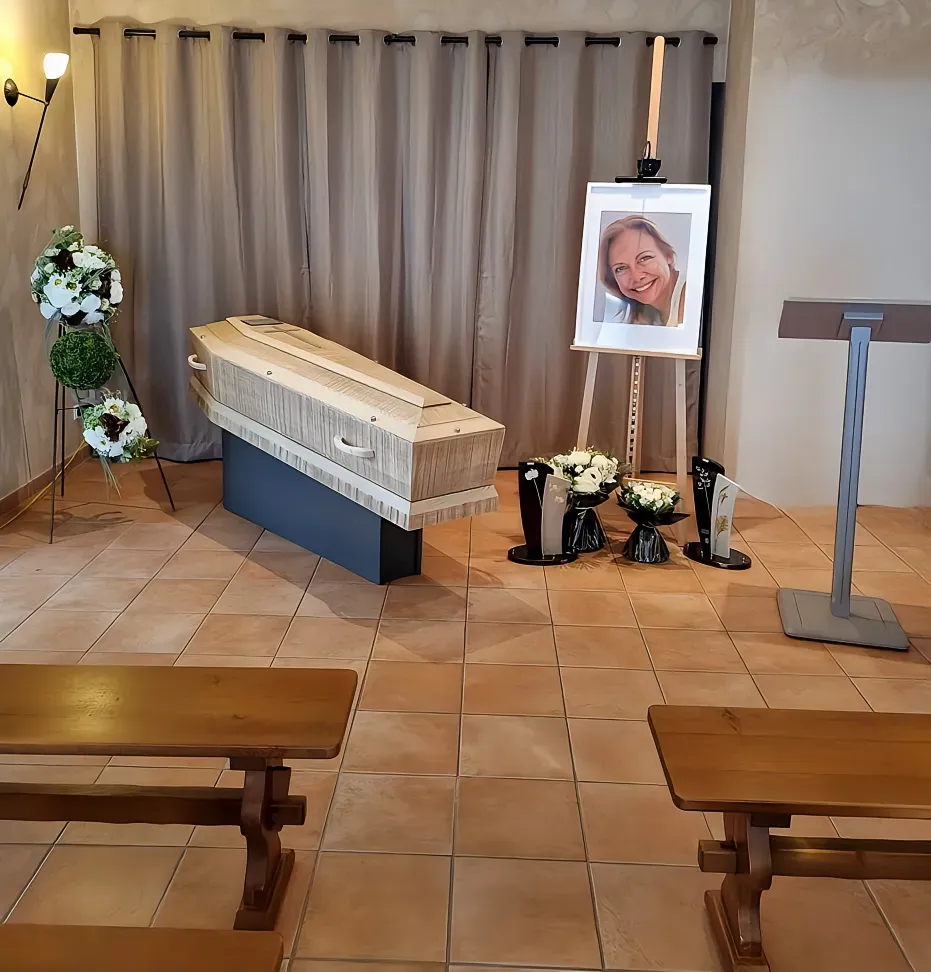 Salle de cérémonie funéraire avec cercueil, portrait et bancs en bois.
