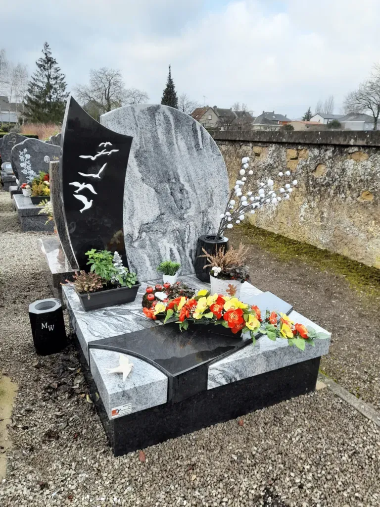 Monument funéraire bicolore en granit noir et gris avec gravure d'oiseaux et fleurs.