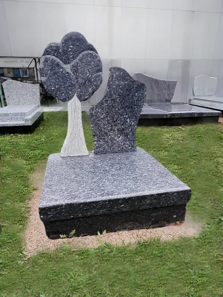 Pierre tombale en granite moucheté avec stèle sculptée en forme d'arbre.
