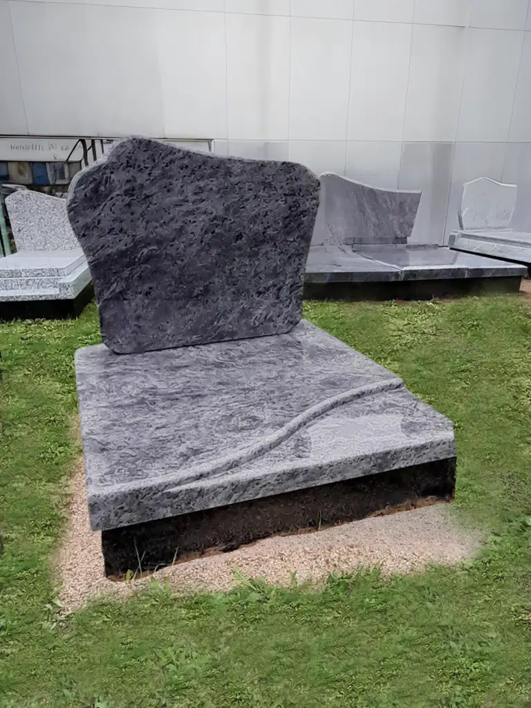 Pierre tombale en granite gris bleu avec stèle asymétrique et sculpture de vagues.